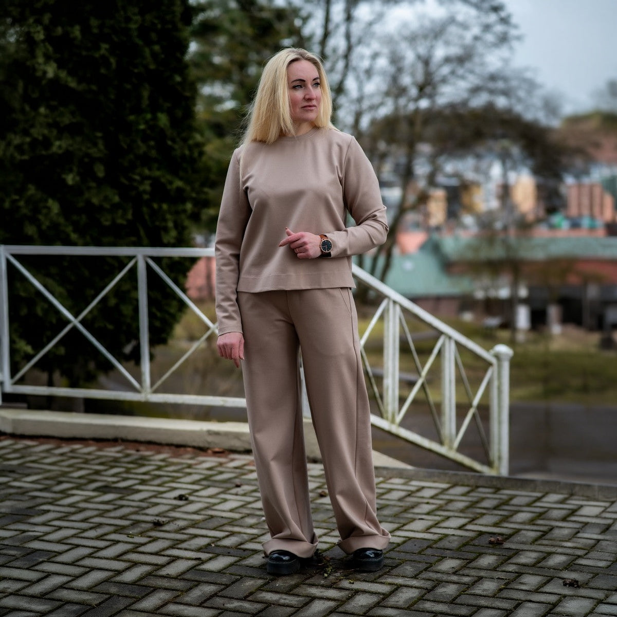 Kreminės spalvos laisvalaikio kostiumėlis moterims ELEGANCIJA. Palaidinė apvalia iškirpte ir platėjančios kelnės su kišenėmis.