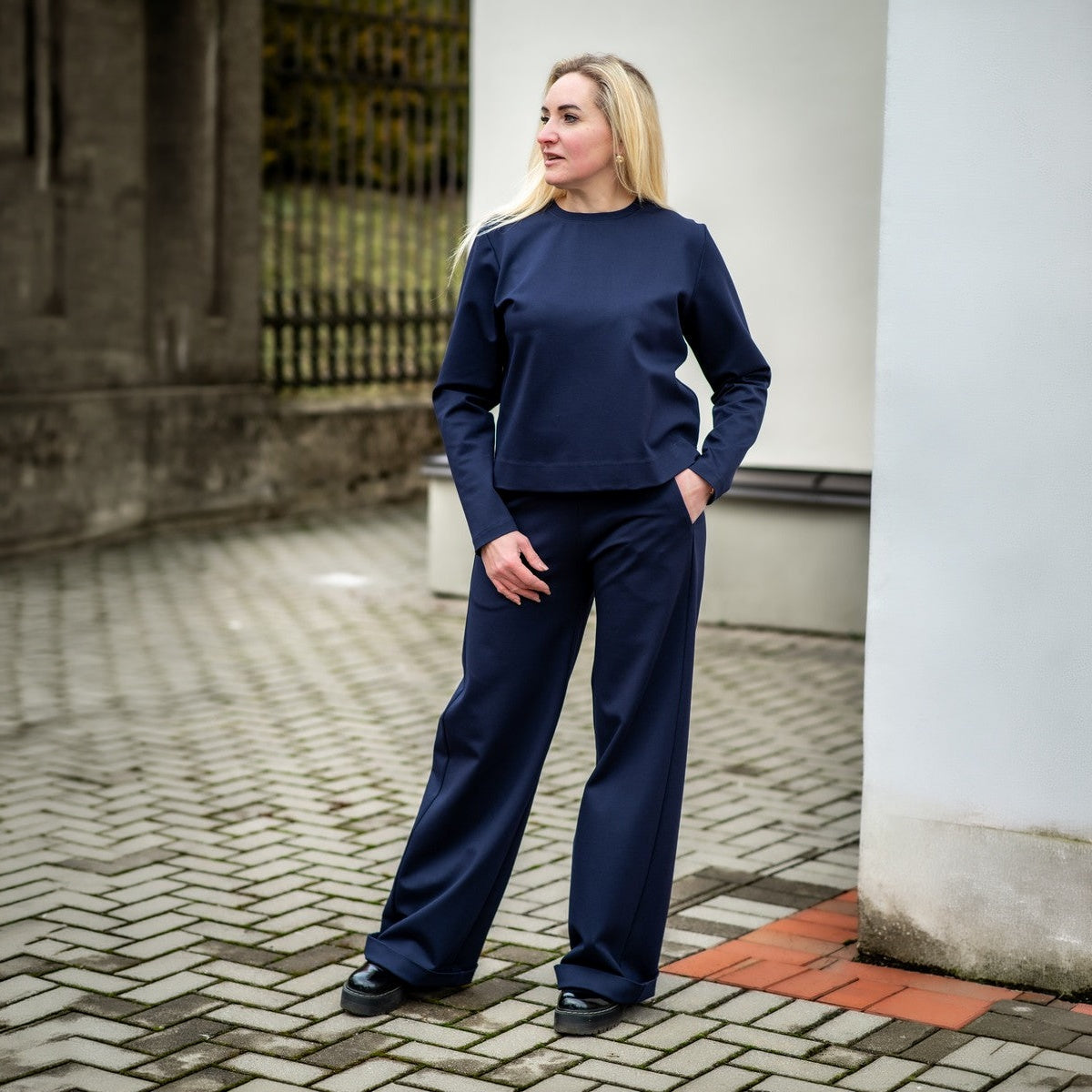 Tamsiai mėlynos spalvos laisvalaikio kostiumėlis moterims ELEGANCIJA. Palaidinė apvalia iškirpte ir platėjančios kelnės su kišenėmis.